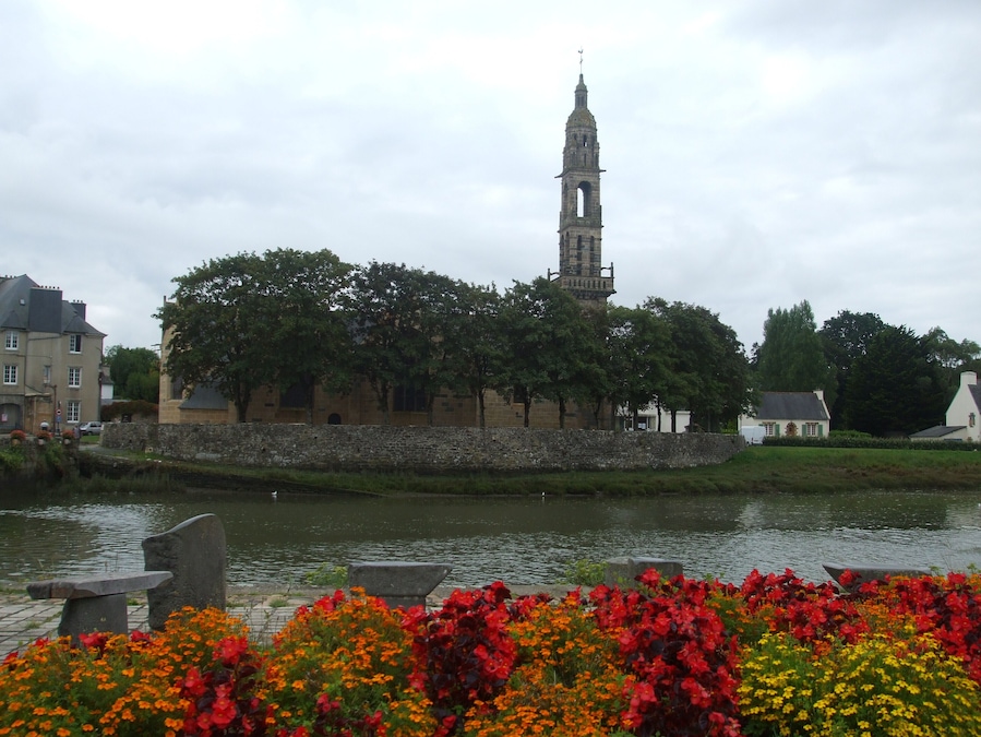 A historic building with a tower, surrounded by trees and a body of water.