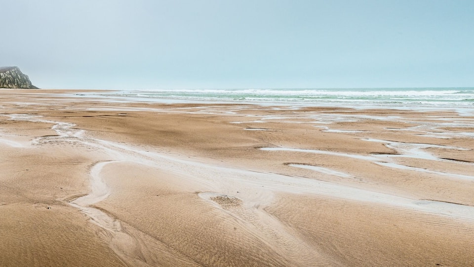 A sandy beach with footprints and a cliff in the background.