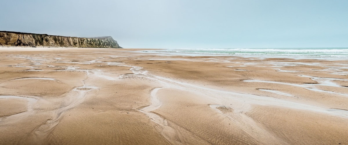A sandy beach with footprints and a cliff in the background.