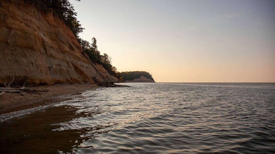 A coastal landscape with a sandy beach, a rocky cliff, and a calm sea.