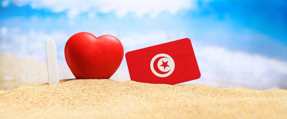 I love Tunisia. Flag of Tunisia on the beach with a red heart. vacation and travel concept.