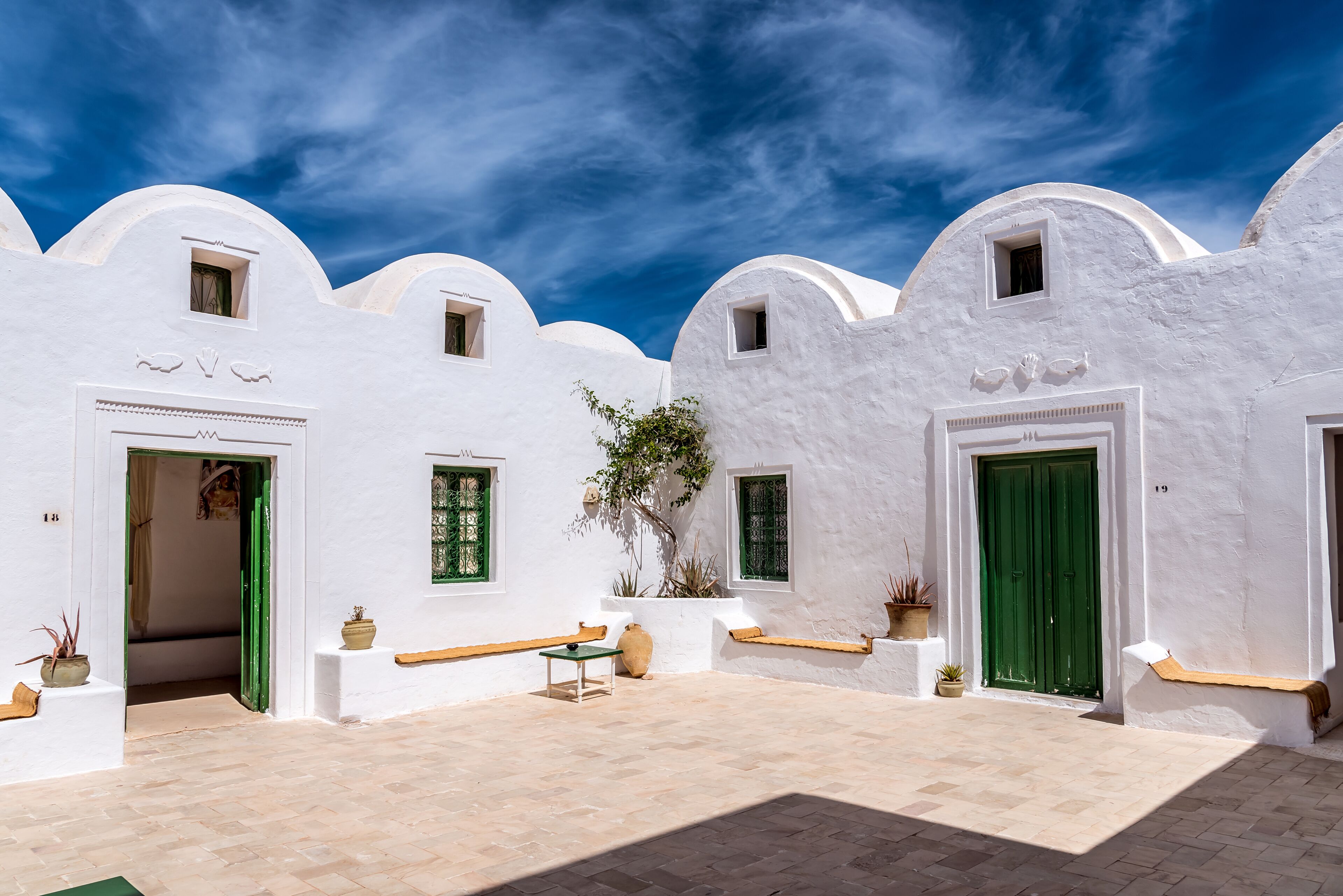 A white-walled courtyard with green doors, potted plants, and a tiled floor.