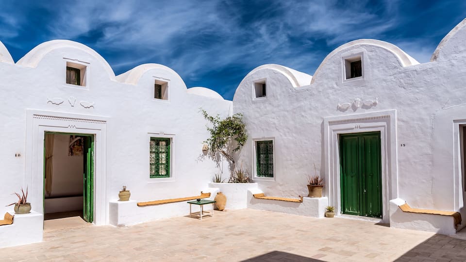 A white-walled courtyard with green doors, potted plants, and a tiled floor.