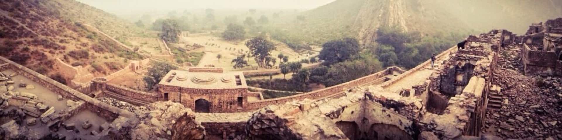 An ancient ruin with a central building, a large mountain in the background, and a valley.