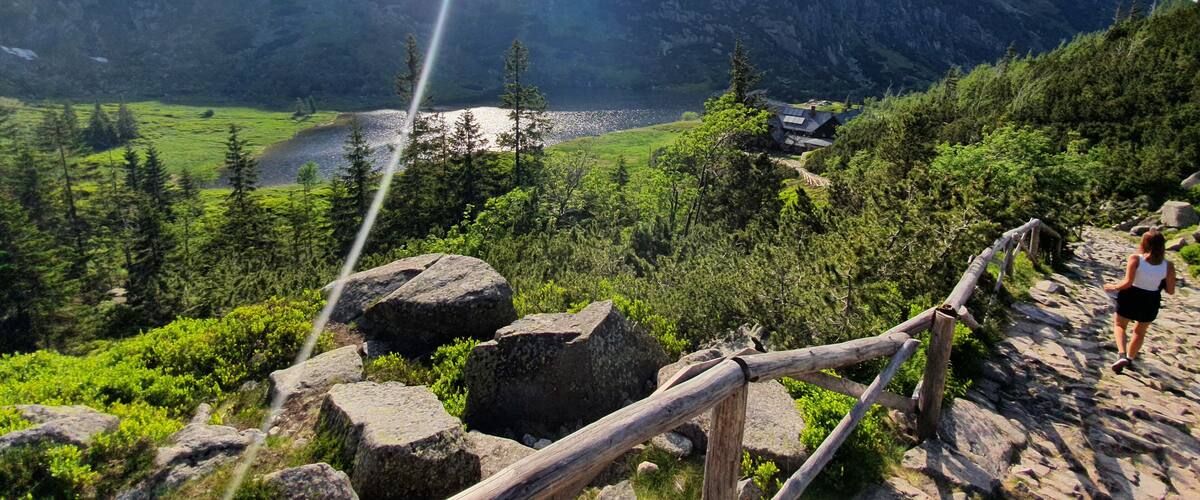 A mountain landscape with a lake, a wooden fence, and a person hiking.