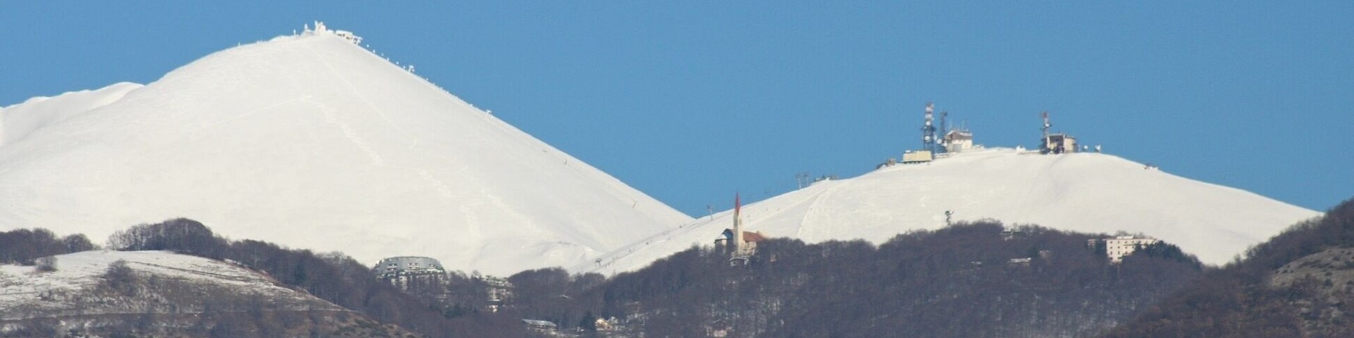 Una montaña nevada con un telesilla y edificios en sus laderas.
