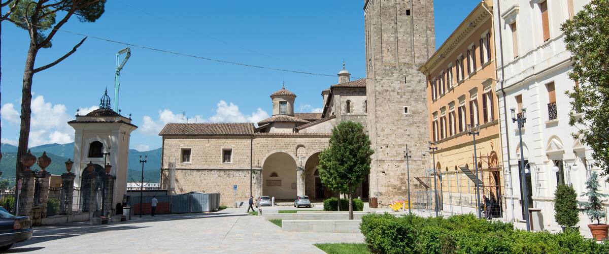 A historic building with a prominent tower, a courtyard, and surrounding greenery.