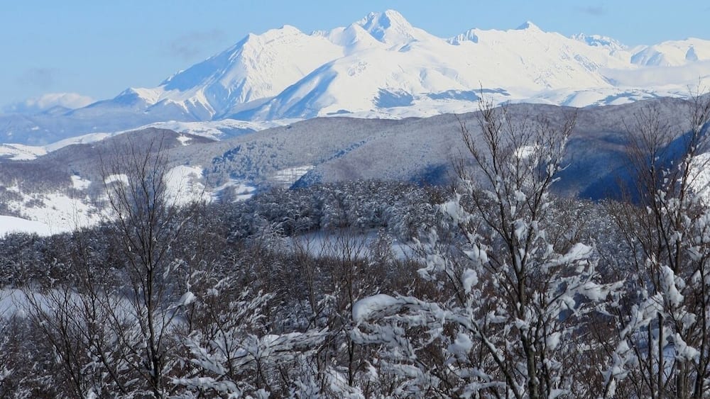 A snow-covered mountain range with a lake in the foreground.
