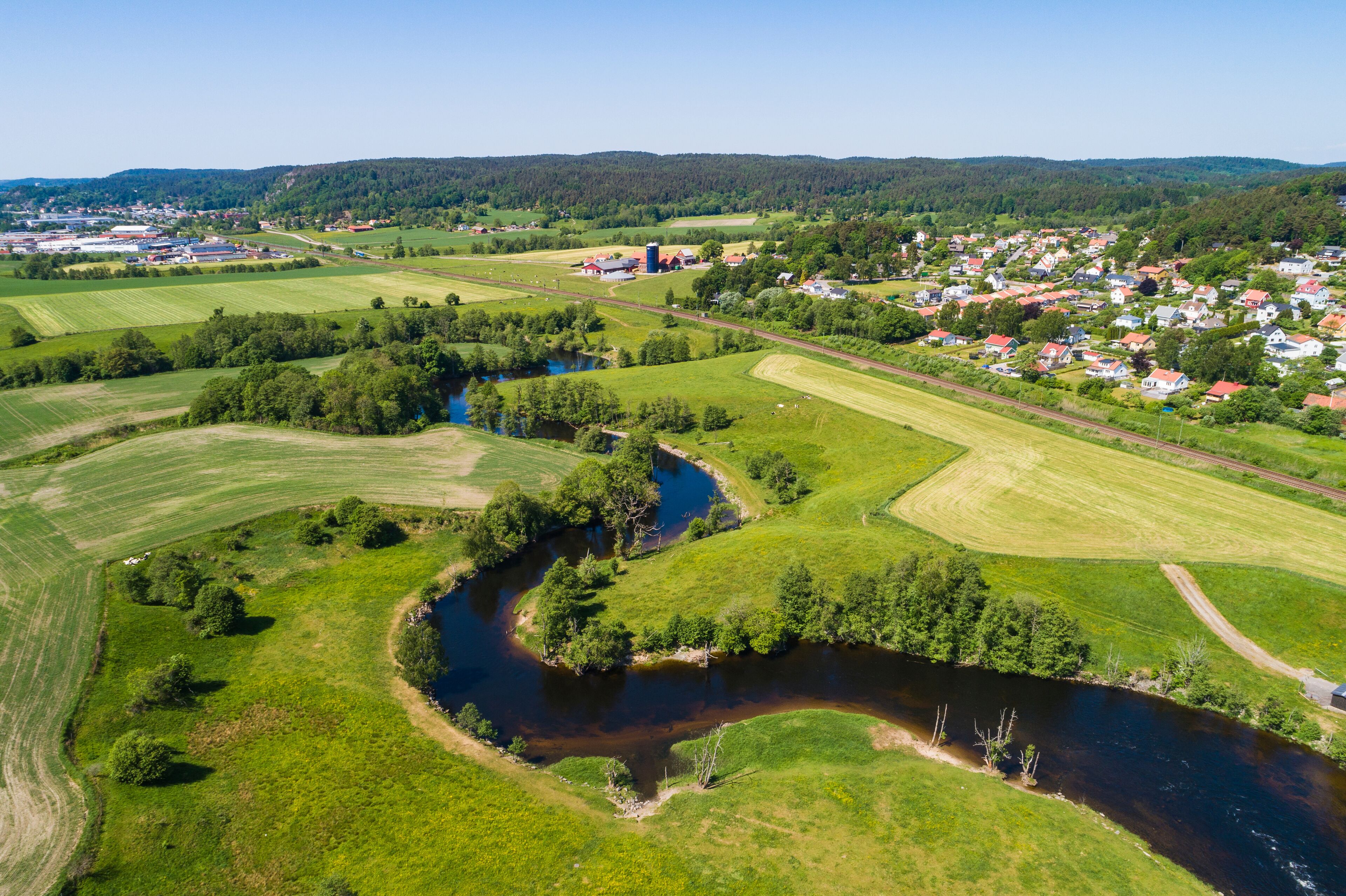 A river winding through green fields, a small town with red-roofed houses, and a distant industrial area.