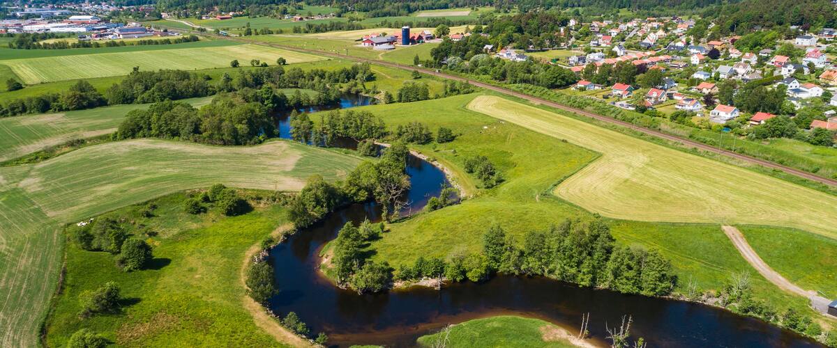 A river winding through green fields, a small town with red-roofed houses, and a distant industrial area.