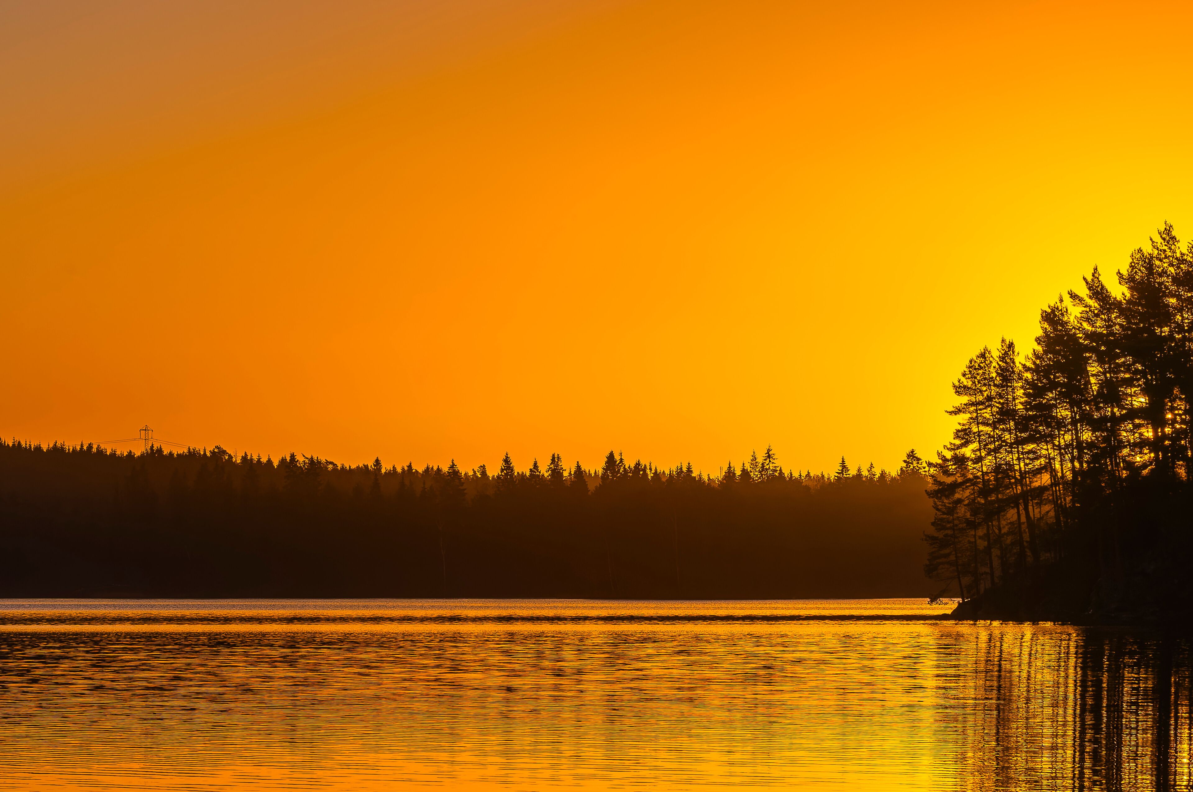 Sunrise at a lake near Gothenburg in Sweden with trees along the shoreline and a bright orange sky