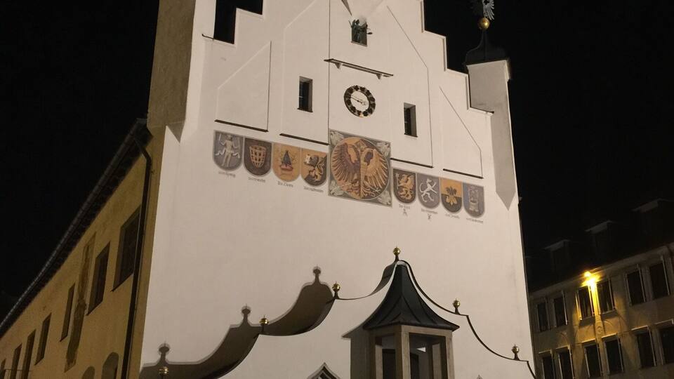 A white building with a clock tower, arched windows, and decorative shields.