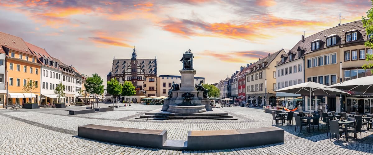 A cobblestone square with a central fountain, surrounded by historic buildings and outdoor seating areas.