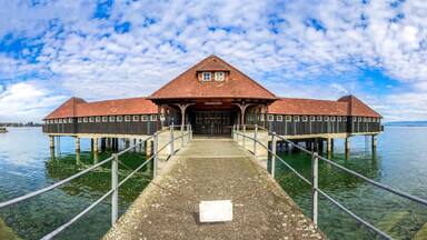 A wooden pier leading to a building with a red roof and a sign that reads "GRABENBACH".