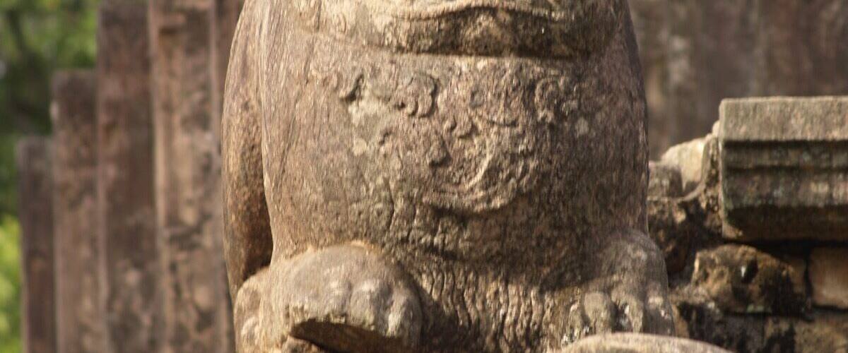 A stone lion statue with a serene expression, surrounded by ancient stone structures.