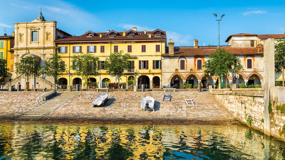 A historic square with a canal, stone steps, and traditional buildings with arched windows and a bell tower.
