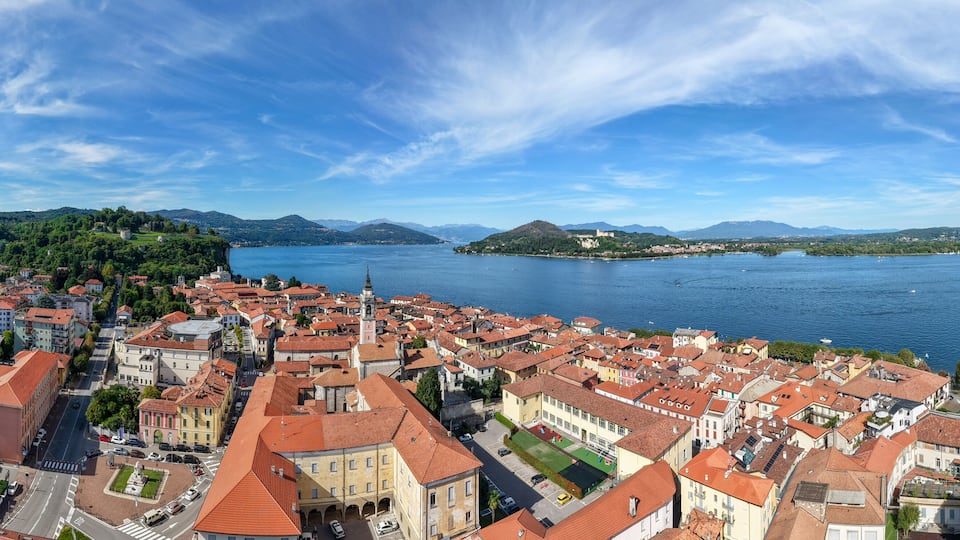 A coastal cityscape with red-roofed buildings, a large body of water, and distant mountains.