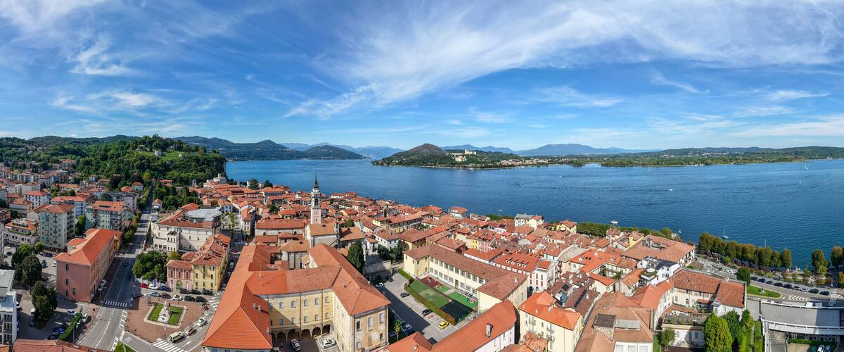 A coastal cityscape with red-roofed buildings, a large body of water, and distant mountains.