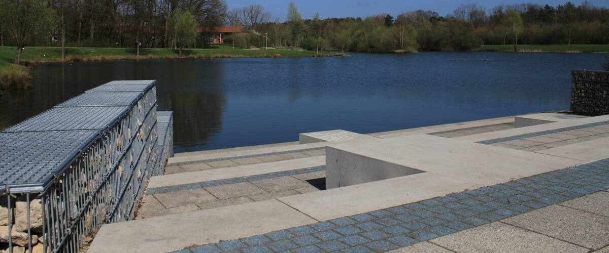 A calm lake with a concrete viewing platform and metal railings.