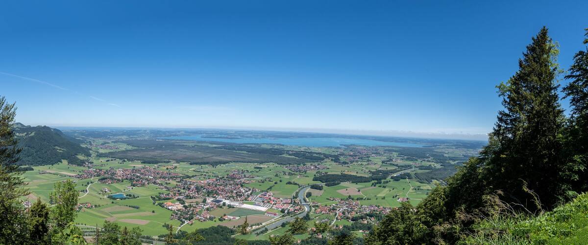 A panoramic view of a town nestled in a valley with a river, surrounded by green fields and hills.
