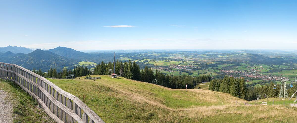 A panoramic view of a mountainous landscape with a wooden fence, a red flag, and a distant town.