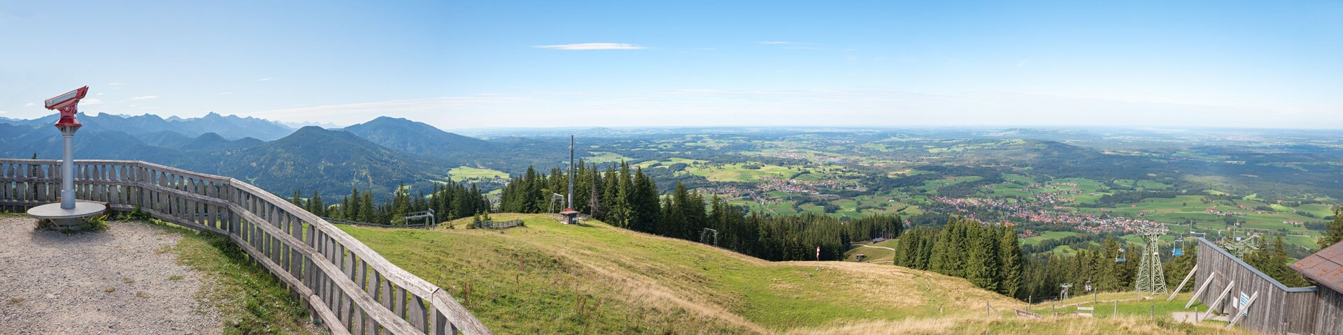 A panoramic view of a mountainous landscape with a wooden fence, a red flag, and a distant town.