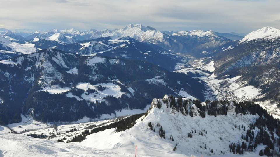 A snow-covered mountain range with a ski slope in the foreground.