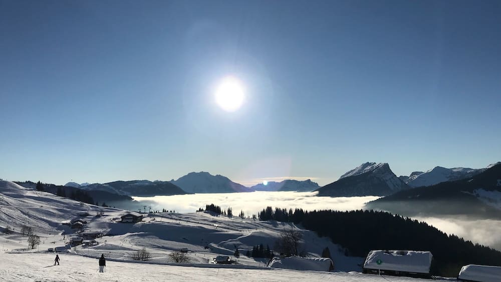 Un paysage de montagne enneigé, avec un ciel dégagé, un soleil éclatant et une vallée en contrebas.