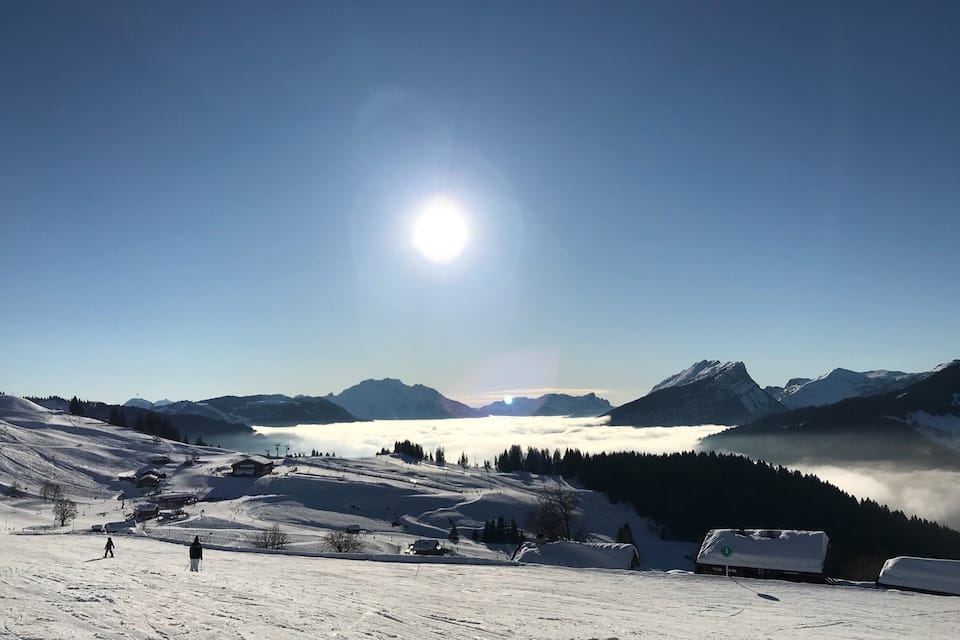 Un paisaje montañoso nevado con cielo despejado, un sol brillante y un valle abajo.
