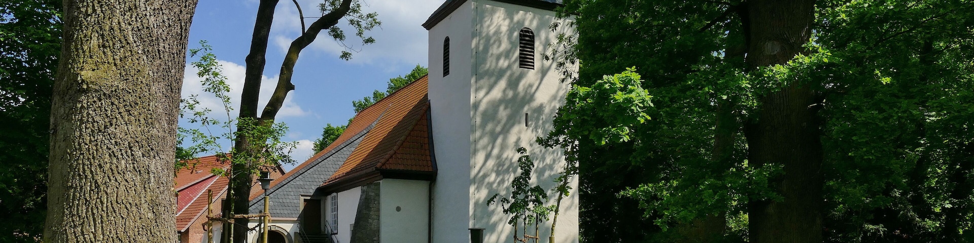 A church with a tall steeple surrounded by trees and a grassy area.