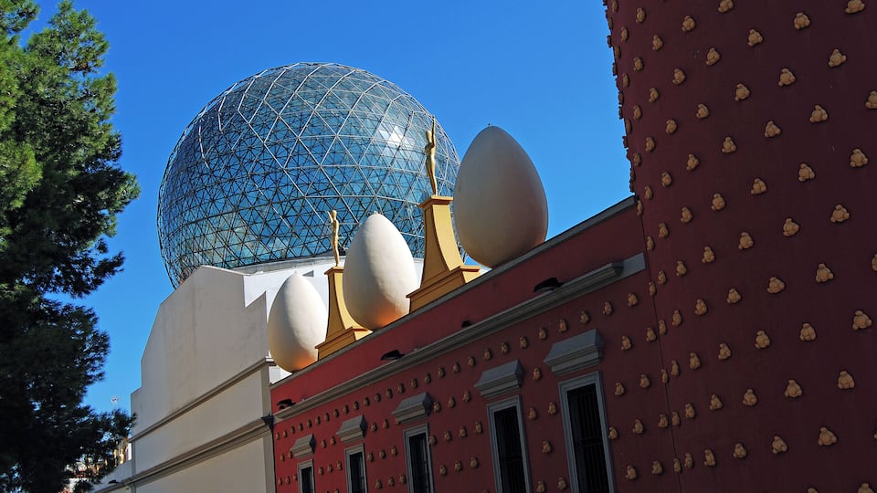 A large glass dome structure atop a building with a red facade and decorative elements.