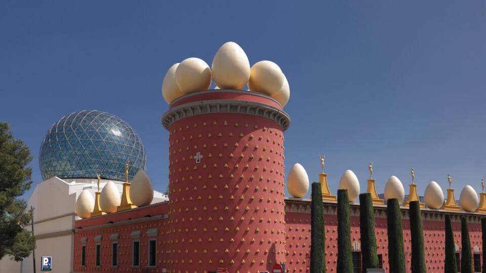 A building with a red facade, a large dome, and multiple golden statues.