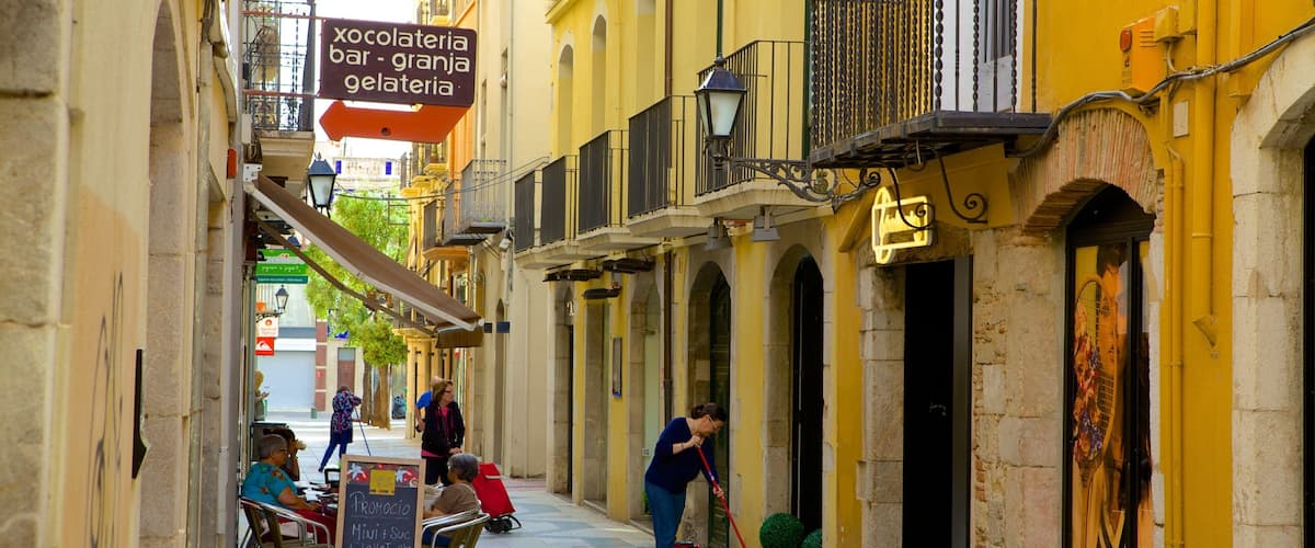 A narrow street with yellow buildings, a sign for a chocolate shop, and a person sweeping the pavement.