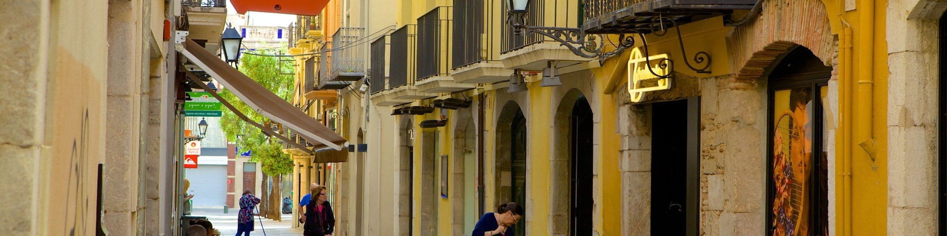 A narrow street with yellow buildings, a sign for a chocolate shop, and a person sweeping the pavement.