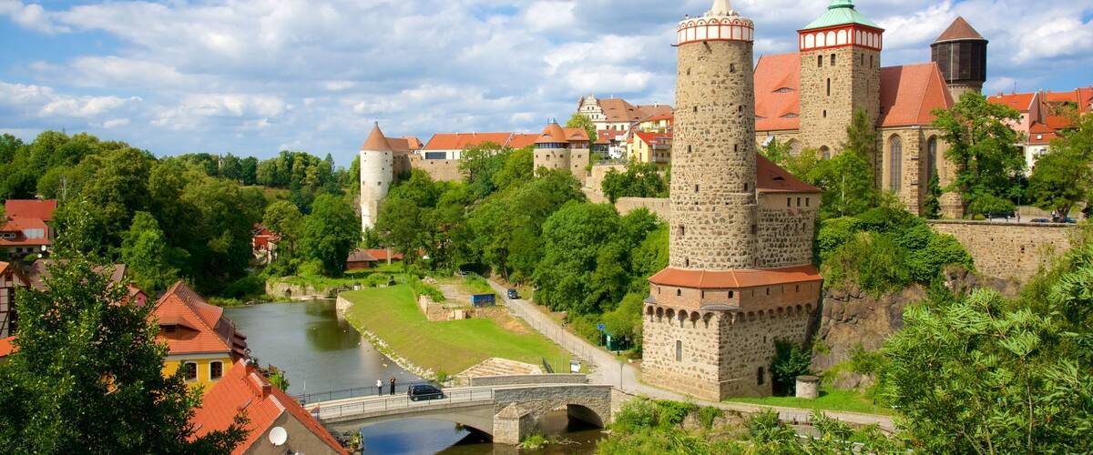 A historic castle with a prominent tower, a river, and lush greenery.