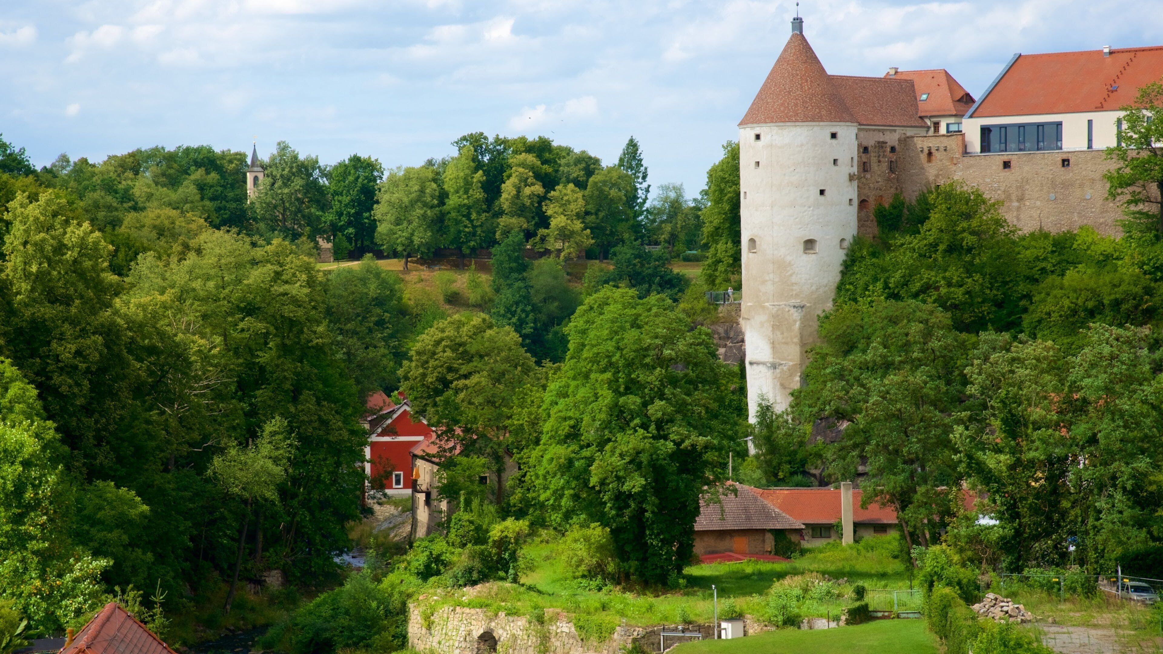 A castle on a hill with surrounding greenery and a river.