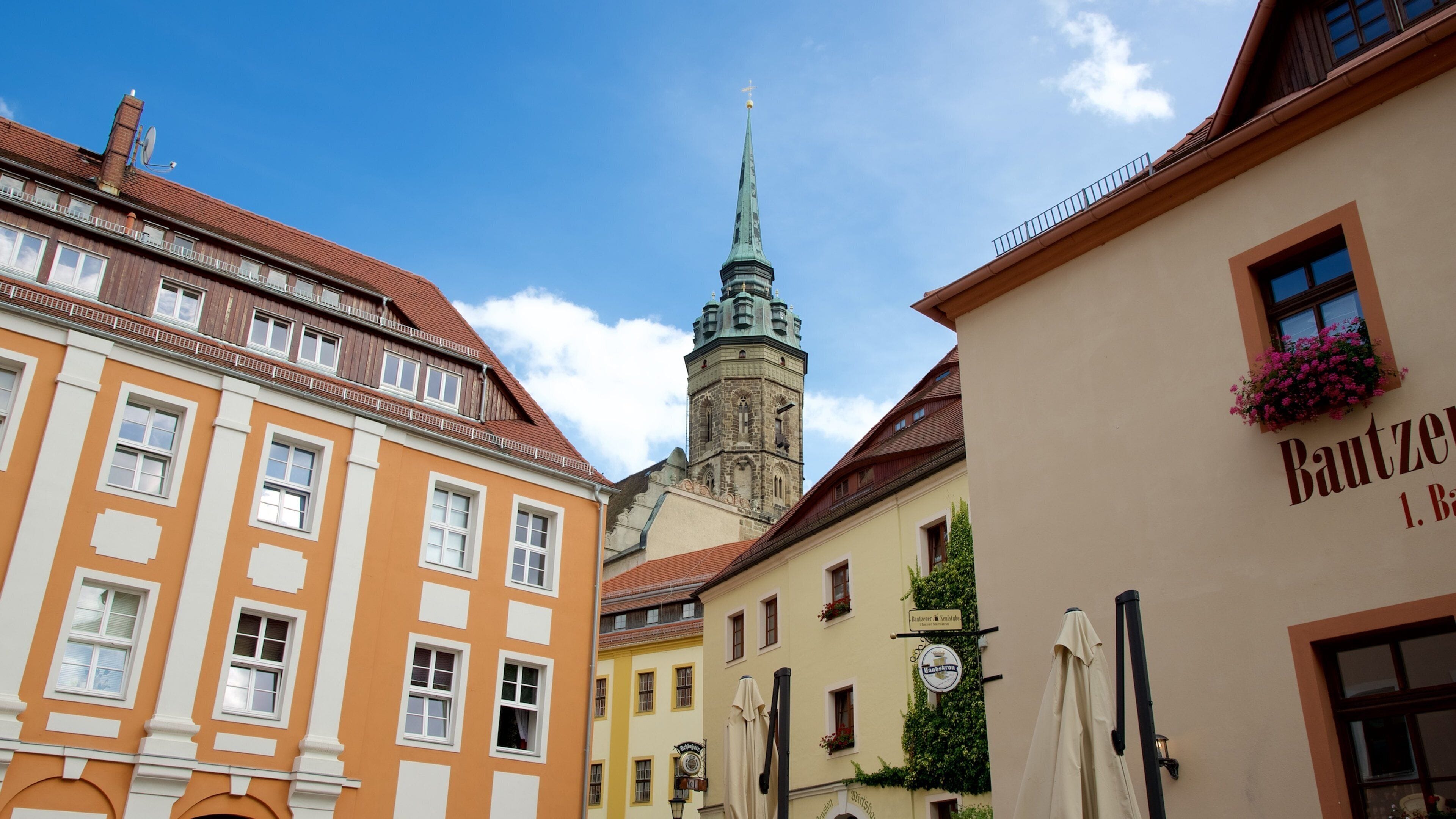 A street with historic buildings, a church tower, and a sign for "Bautzen 1. B".