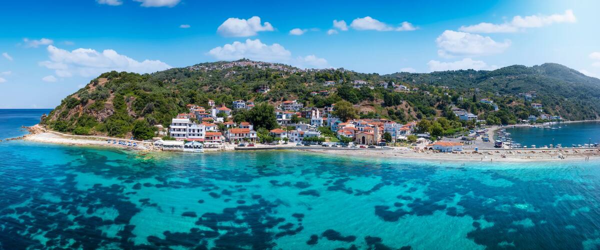 A coastal town with buildings on a hillside, clear turquoise waters, and a sandy beach.