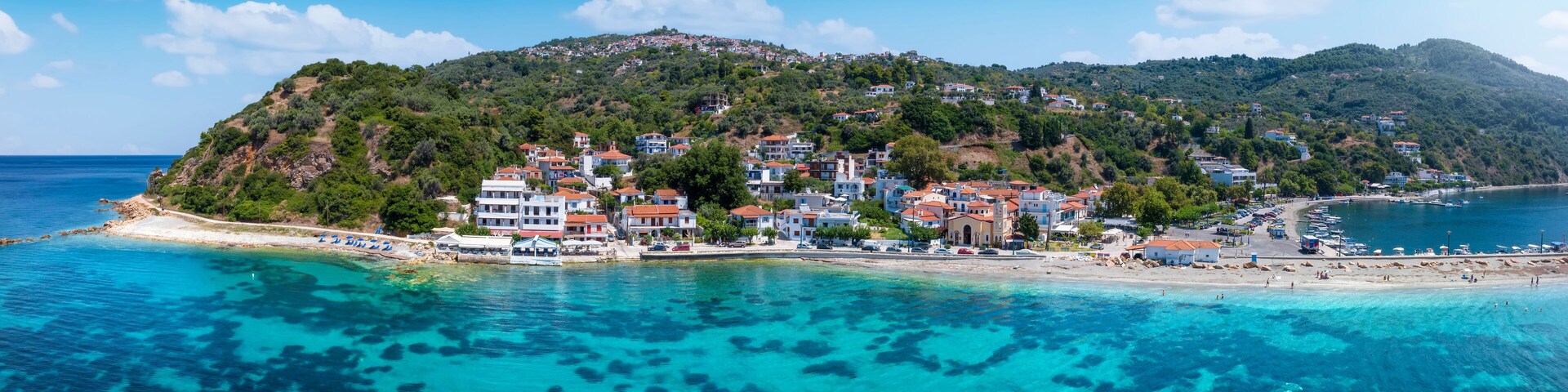 A coastal town with buildings on a hillside, clear turquoise waters, and a sandy beach.
