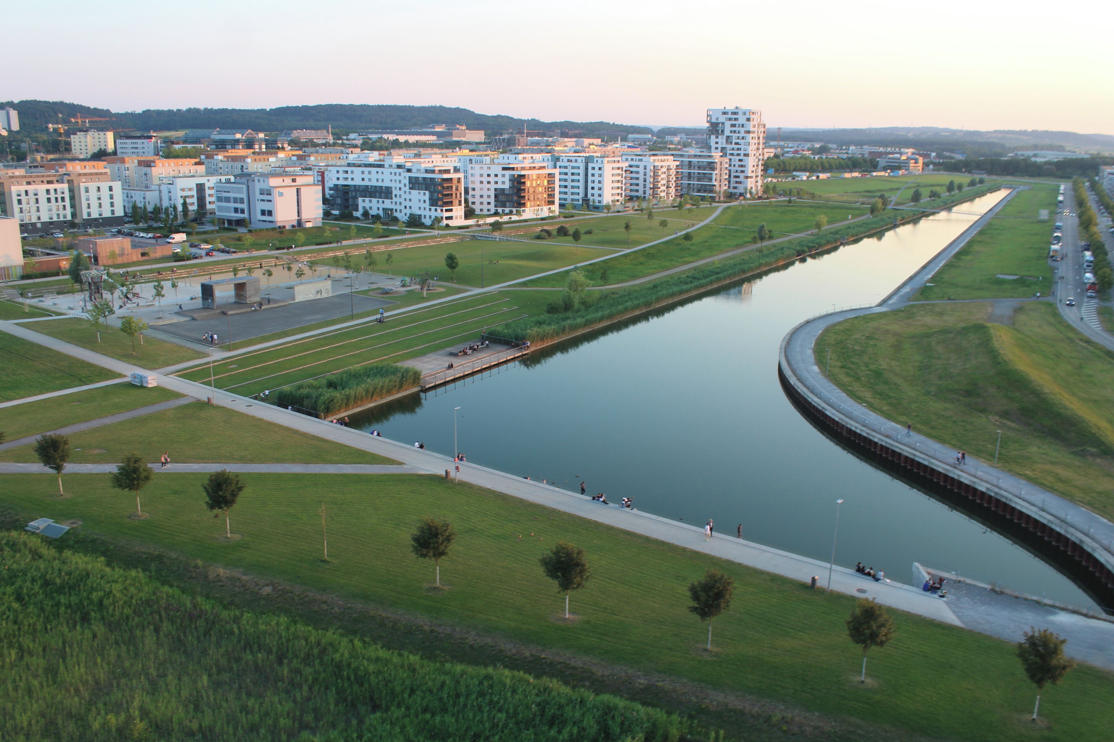 A river with a bridge, a park with trees, and modern buildings in the background.