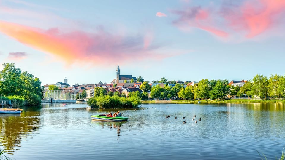 A calm lake with boats, a church, and surrounding greenery.