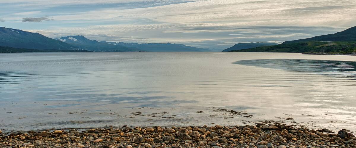 A calm lake with a rocky shoreline and mountains in the background.
