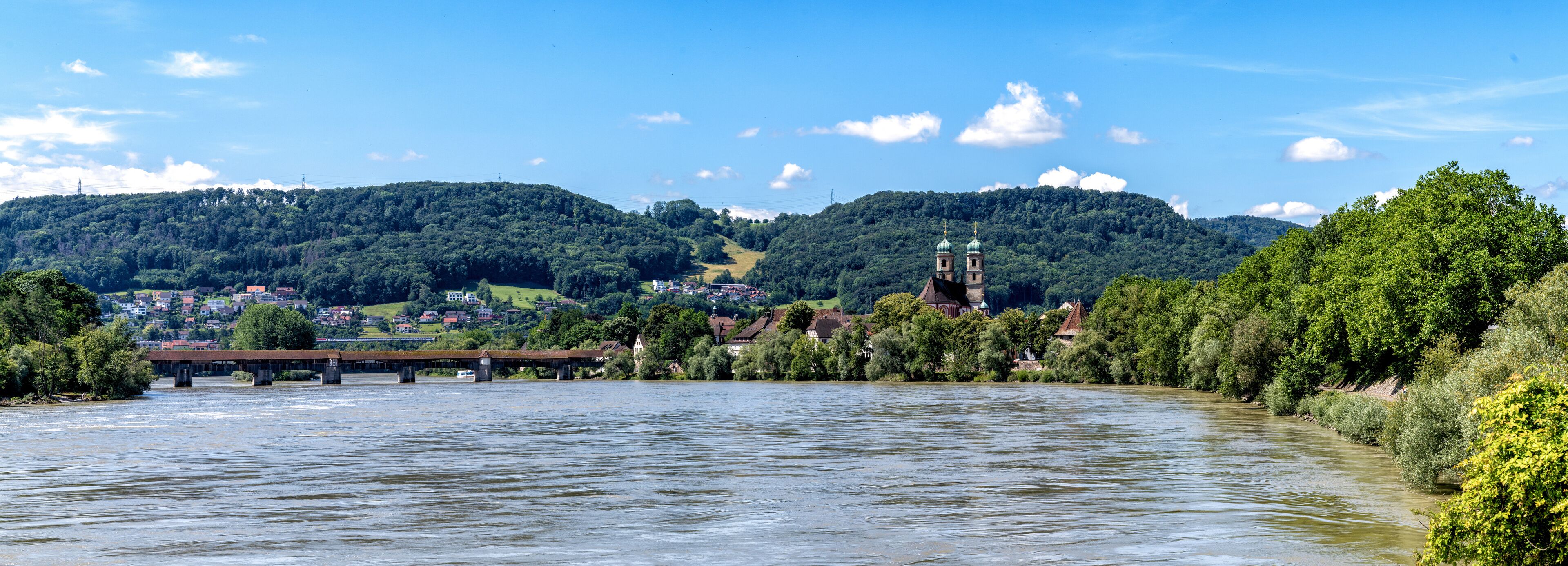 A river with a bridge, a church, and a town surrounded by hills.