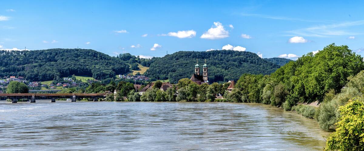 A river with a bridge, a church, and a town surrounded by hills.
