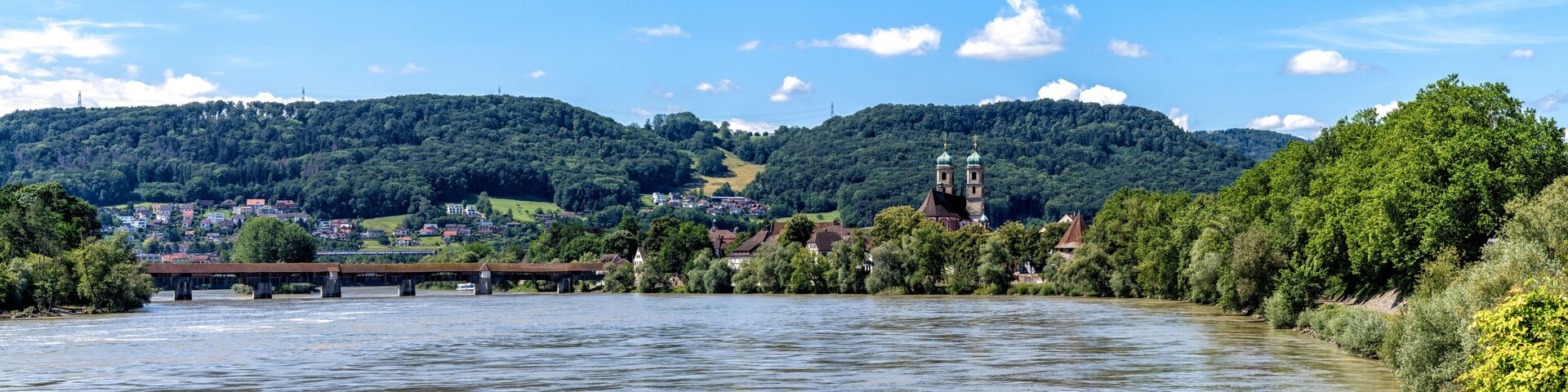 A river with a bridge, a church, and a town surrounded by hills.