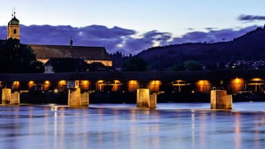 Un pueblo a orillas del río al anochecer, con edificios iluminados y una torre de iglesia.