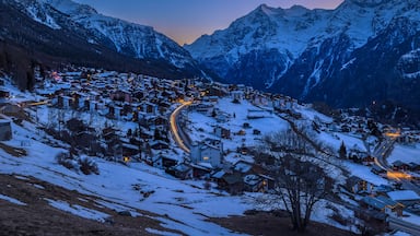 A snow-covered mountain village at dusk with illuminated buildings and winding roads.
