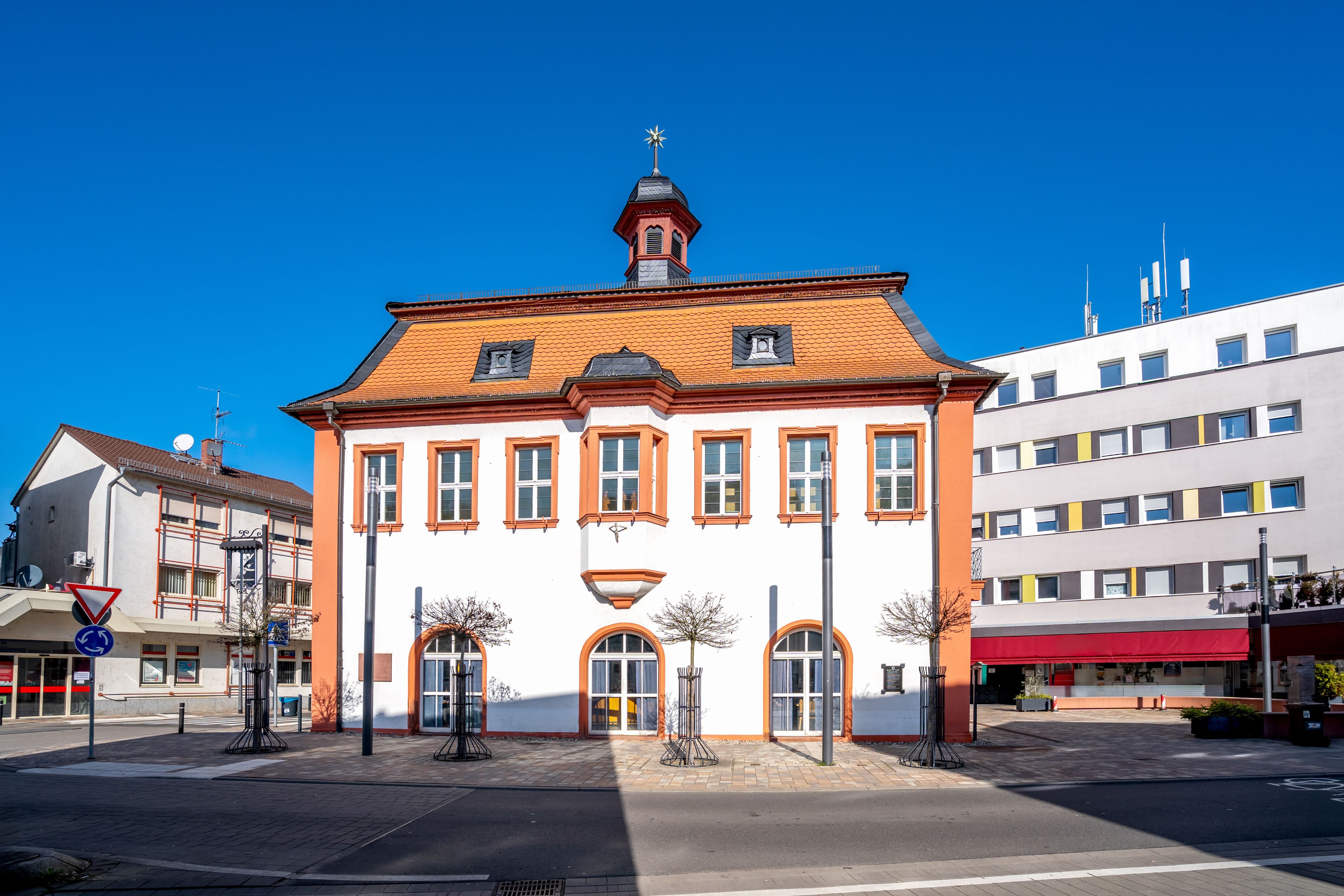 Um edifício histórico com telhado de telhas vermelhas e torre do relógio, cercado por edifícios modernos.