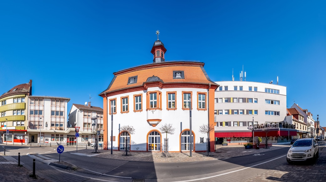 Um edifício circular com telhado vermelho e torre do relógio, rodeado por edifícios modernos.