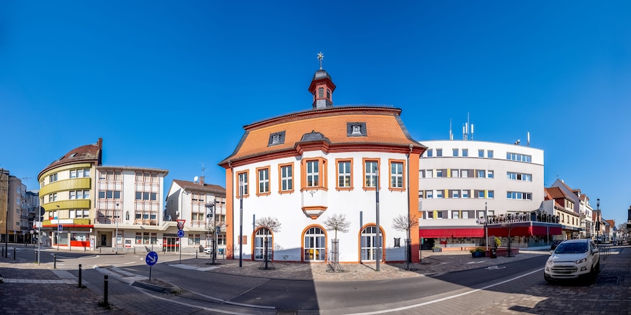 A round building with a red roof and a clock tower, surrounded by modern buildings.